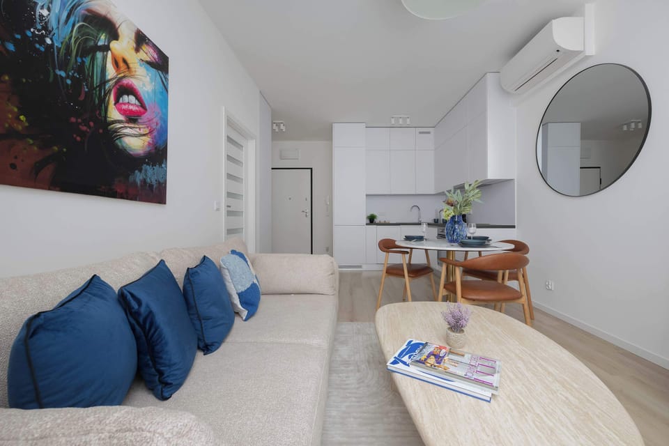 A living room with a comfortable sofa, pillows, and a round coffee table. A dining table and chairs are situated behind the sofa.