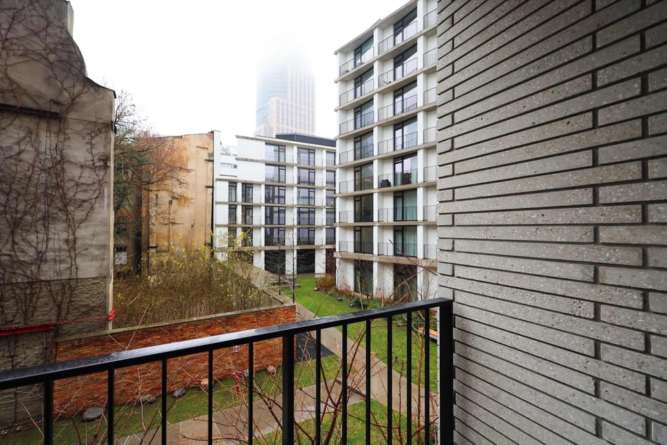 A balcony view with railing and surrounding buildings. The outdoor space provides a quiet spot to enjoy fresh air.