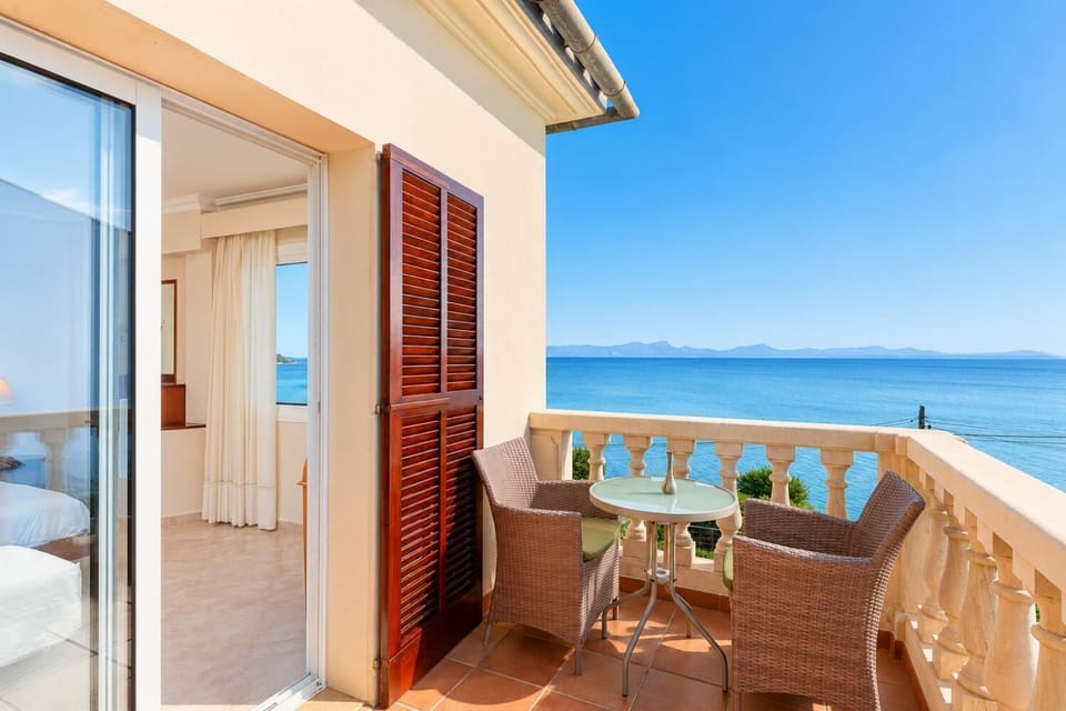 A cozy outdoor seating area with two wicker chairs and a bistro table, opening directly from a bright bedroom.