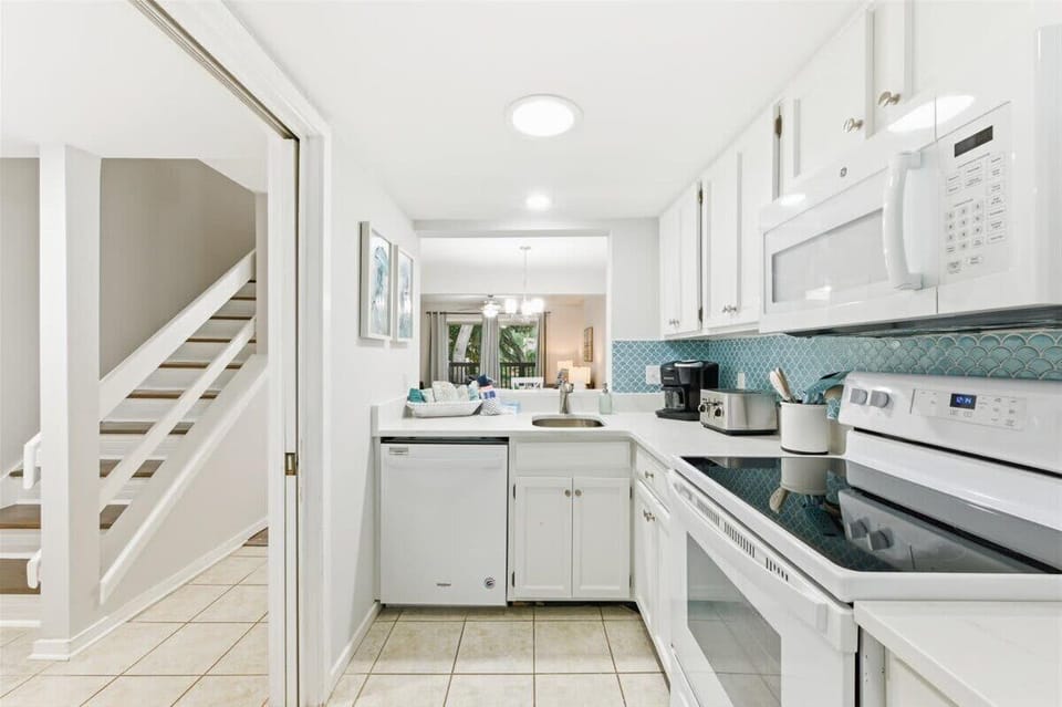 Bright, coastal kitchen with full-size appliances, coffee maker, and blue tile splash.