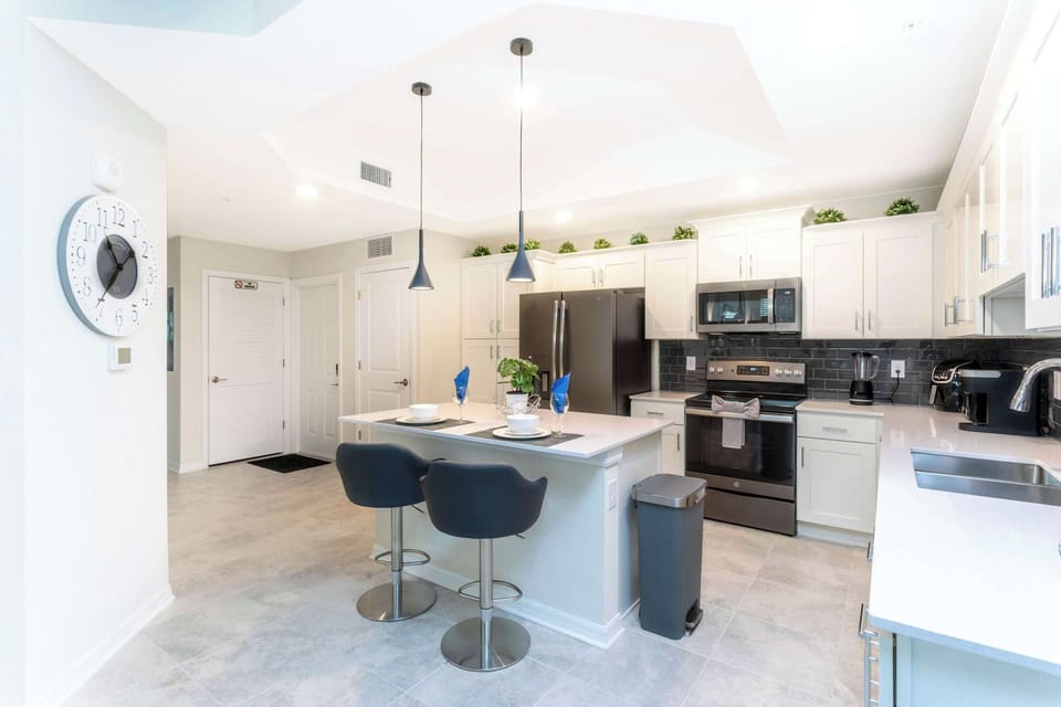 Sleek chef's kitchen with quartz counters, white shaker cabinets, subway tile, and modern appliances. Island seating for 2 under chic pendants-perfect for morning coffee.