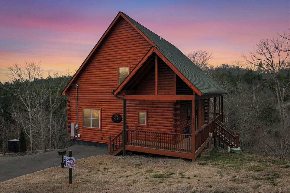 Charming log cabin nestled in wooded surroundings, captured during a stunning sunset with purple and pink skies.