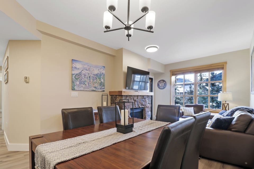 Relax in your open-plan living and dining area featuring a cozy stone fireplace, modern chandelier, and comfortable seating for memorable evenings together.