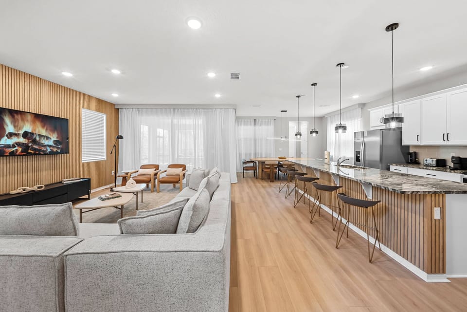 Welcome to a bright living area that blends sleek design and comfort, featuring a cozy sofa and stylish wooden accents. The open layout flows into a modern kitchen, where elegant pendant lights illuminate the spacious counter.