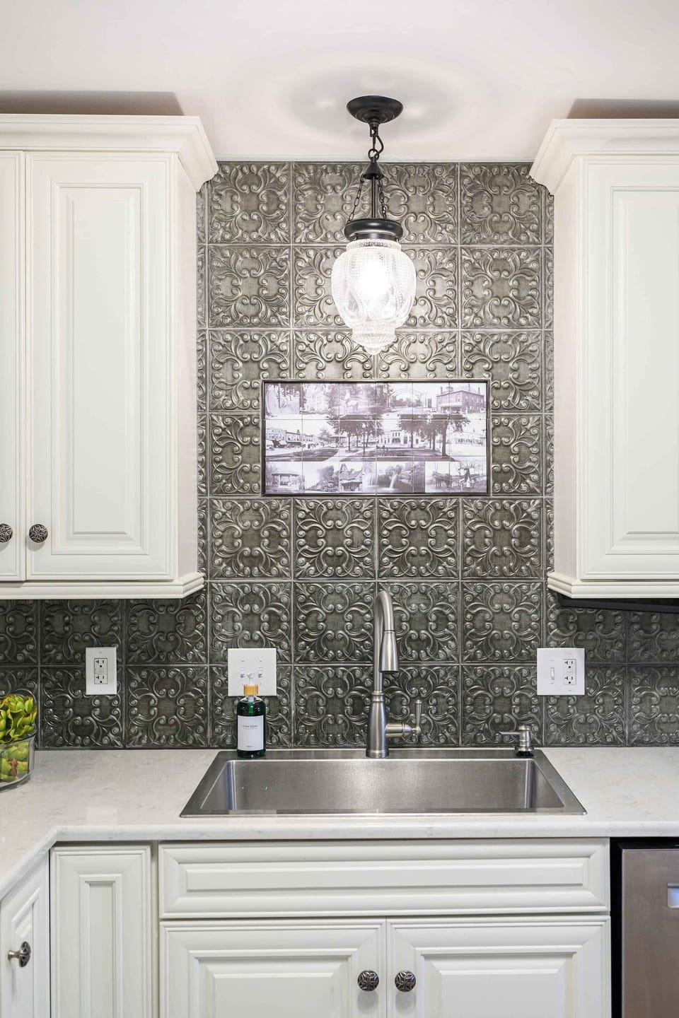 Inviting kitchen sink area highlighted by elegant patterned tile, warm lighting, and crisp white cabinetry.