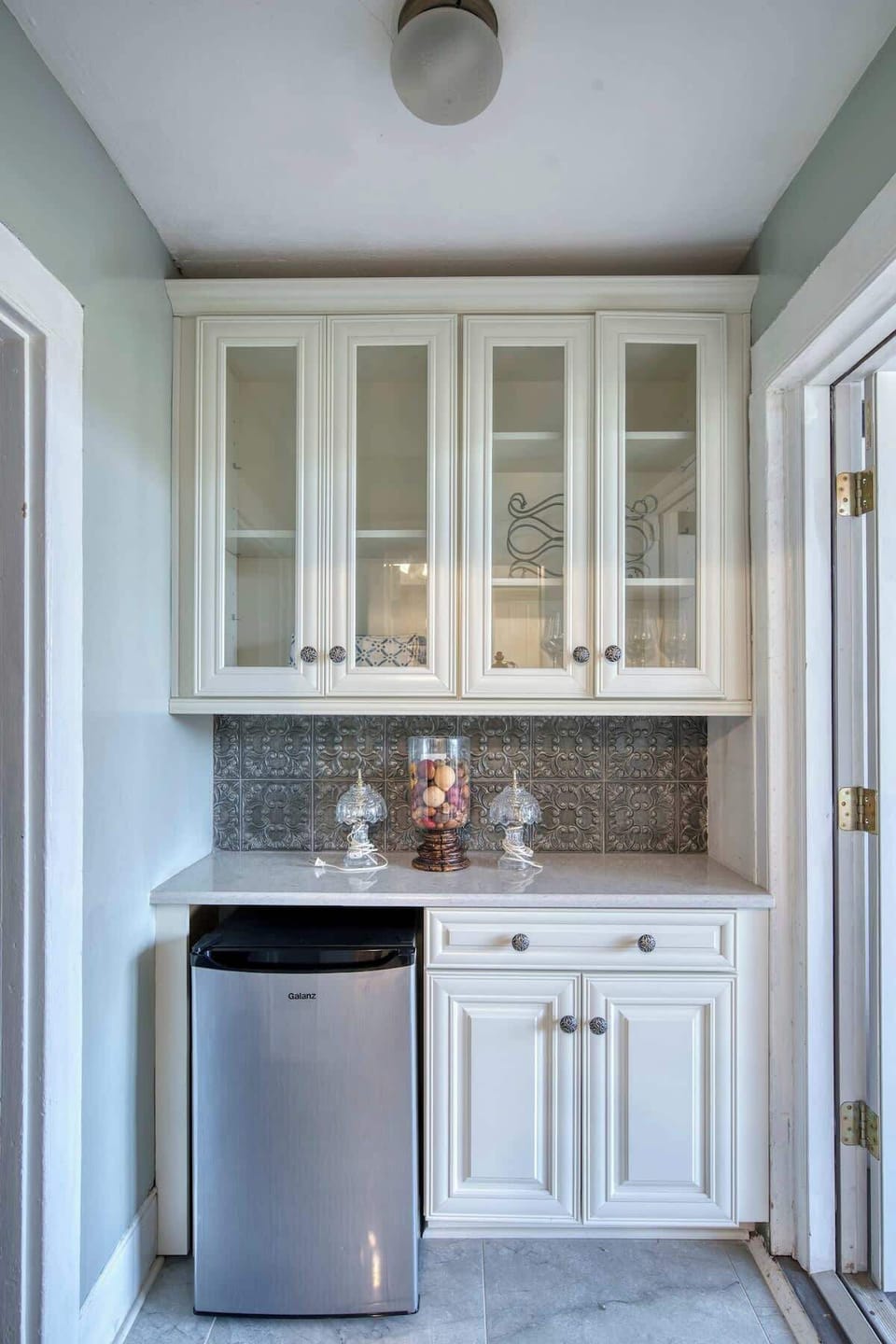 Chic built-in beverage nook with glass-front cabinets, elegant tile backsplash, and a sleek stainless mini fridge.