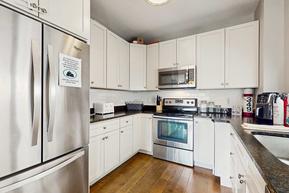 Fully equipped kitchen with white cabinets, stainless steel appliances, microwave, stove, and refrigerator.