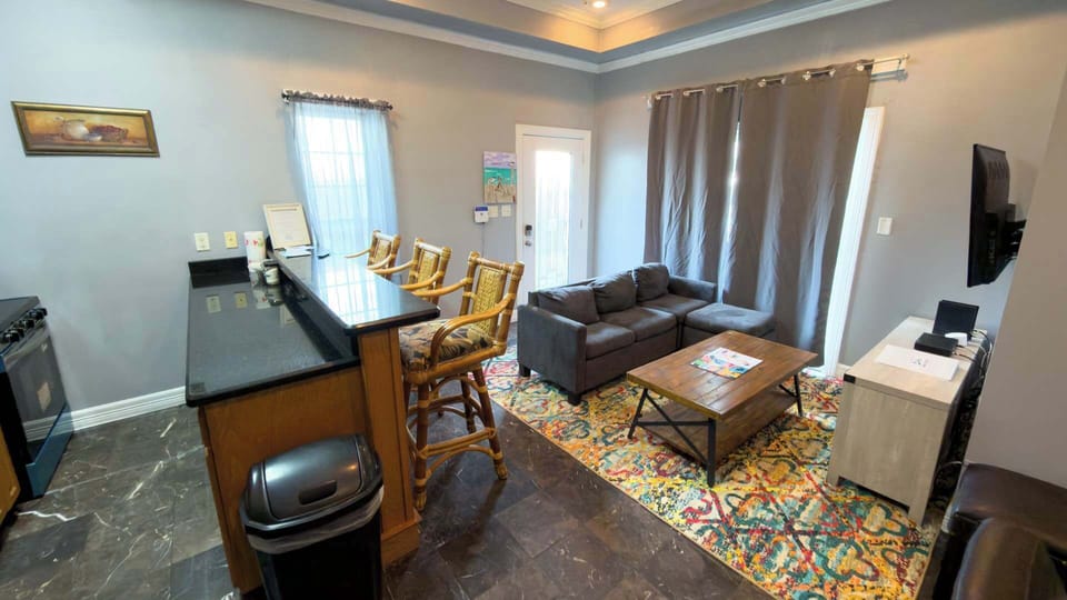 Spacious Living & Kitchen Combo
Gather in a welcoming open-plan space with comfy gray sofa, smart TV, granite breakfast bar with stools, and full kitchen, perfect for casual meals, family hangouts, or streaming beach evenings.