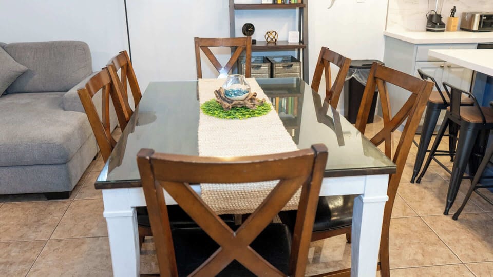 Bright Open Kitchen & Dining Retreat.
Spacious white shaker cabinets, stainless appliances, navy island flow into wood farmhouse table seating 6 under industrial pendant lights. Cozy gray sofa, plants, lamps—ideal for family meals.