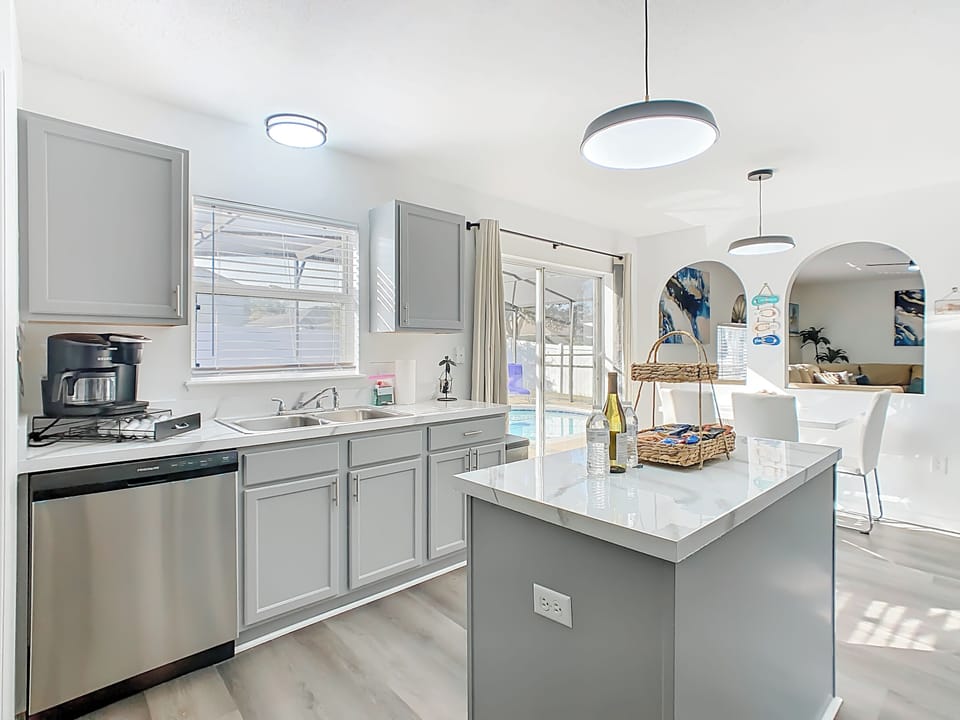 Sunlit kitchen w/ sleek gray cabinets & island breakfast bar.