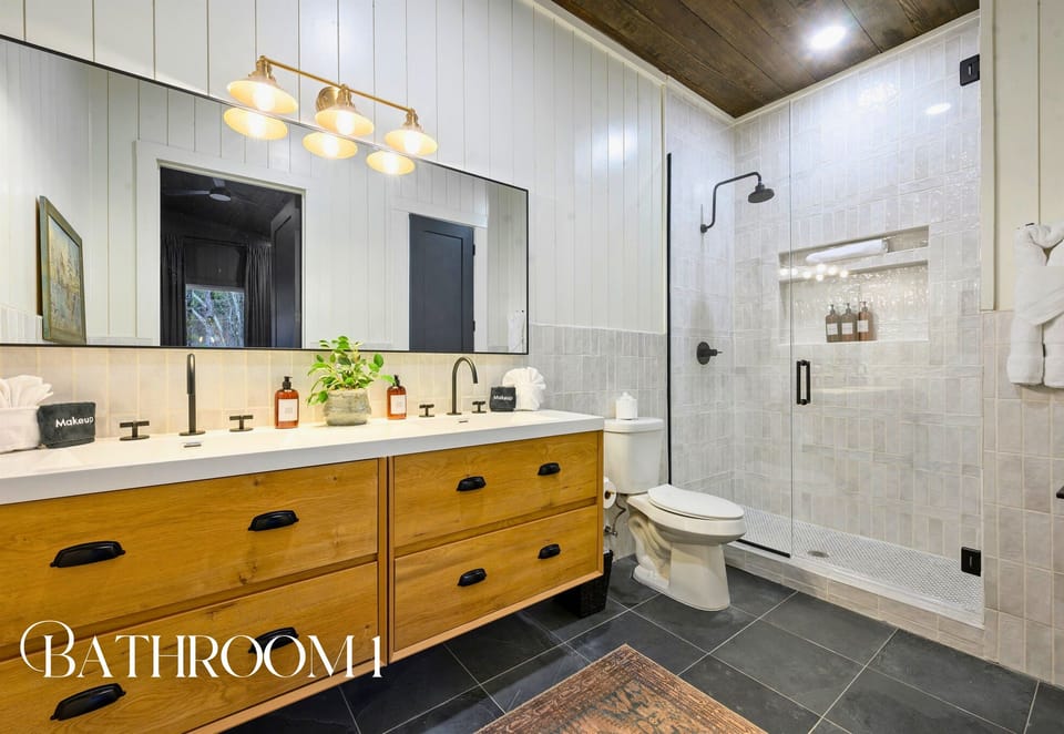 The attached bathroom offers a modern double vanity, a spacious shower, and soothing natural finishes.