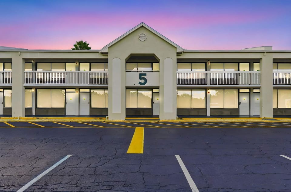 Exterior view of a two-story motel building with ample parking and a colorful sunset sky