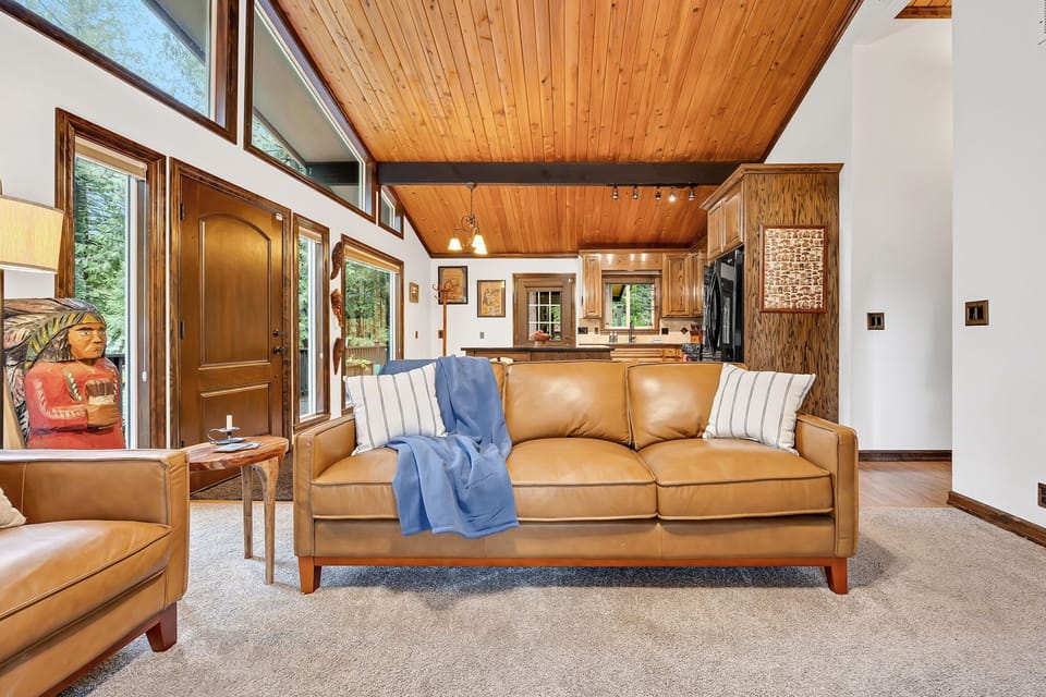 Relax in this sunlit living area with vaulted ceilings, cozy sofa, and warm, inviting cabin design.
