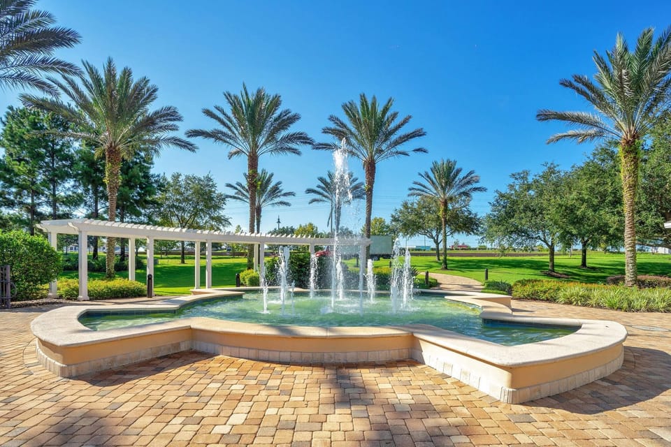 Outdoor fountain surrounded by palm trees and a white pergola in a sunny garden setting