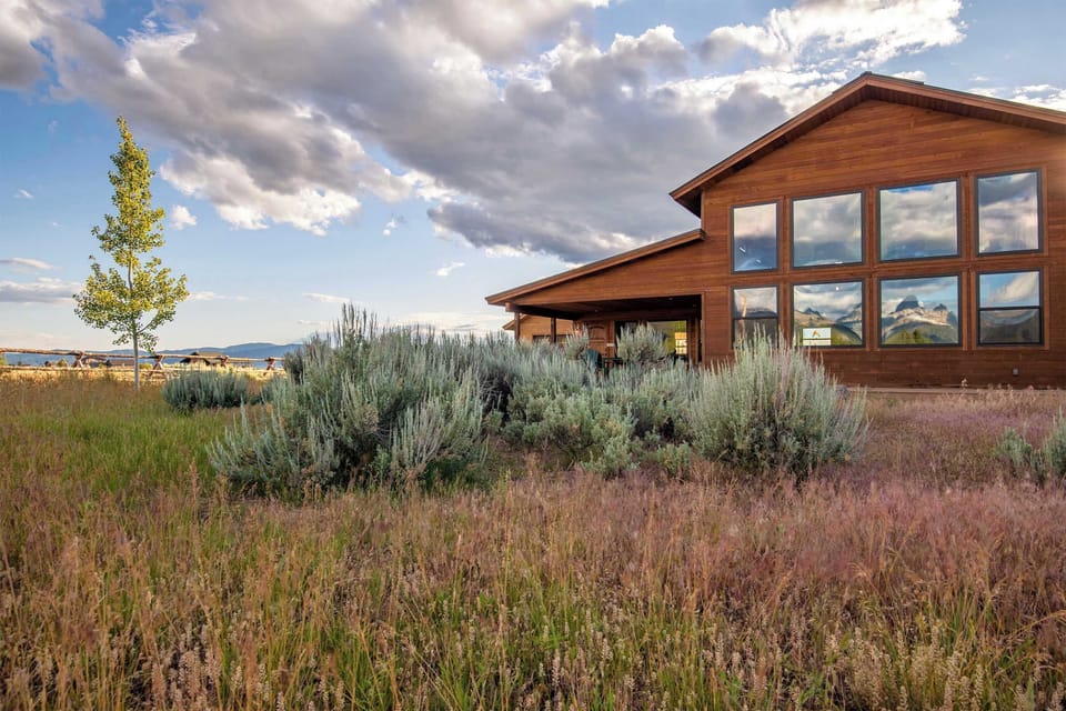 The home from the meadow — clean lines, wide Idaho sky, and Teton peaks on the horizon