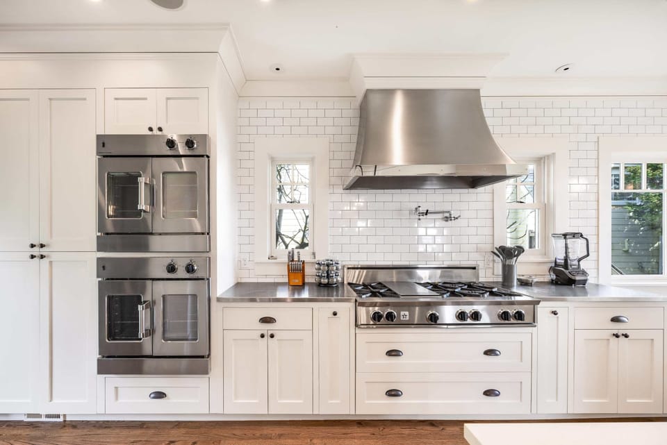 A high-end cooking station with stainless steel appliances, including a double oven and six-burner gas range. The white cabinetry and subway tile backsplash create a bright, polished look.