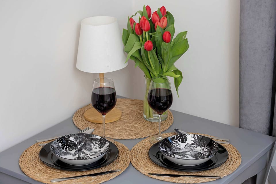 A small dining setup featuring a round table, two place settings, and a vase of red tulips adding color to the room.