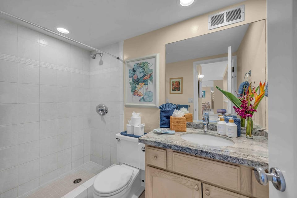 The spacious bathroom features a granite vanity, oversized mirror, walk-in shower, and convenient storage for added comfort. 