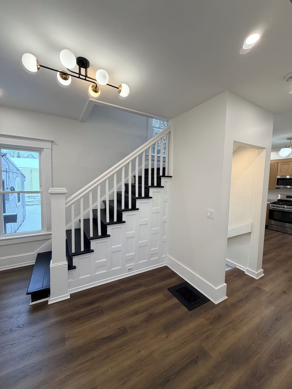 Stairwell to upstairs and down to front door. Glimpse of kitchen. 