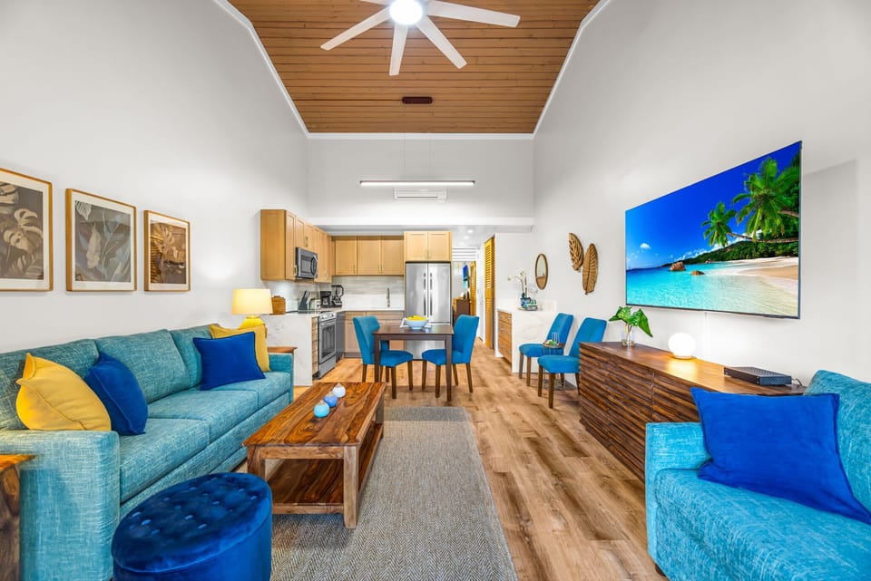 This expansive view highlights the high vaulted ceilings and coastal blue accents that run throughout the home. The open layout seamlessly connects the lounge, dining, and kitchen areas for easy entertaining.