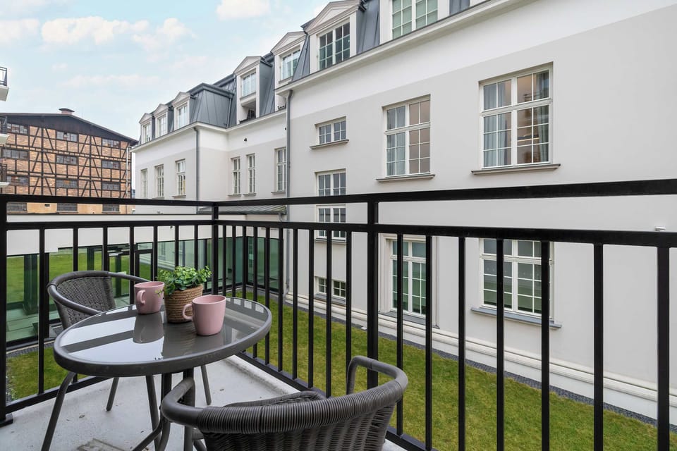 A balcony with a small table and chairs overlooking a courtyard. Metal railings surround the space. The area is ideal for outdoor relaxation.