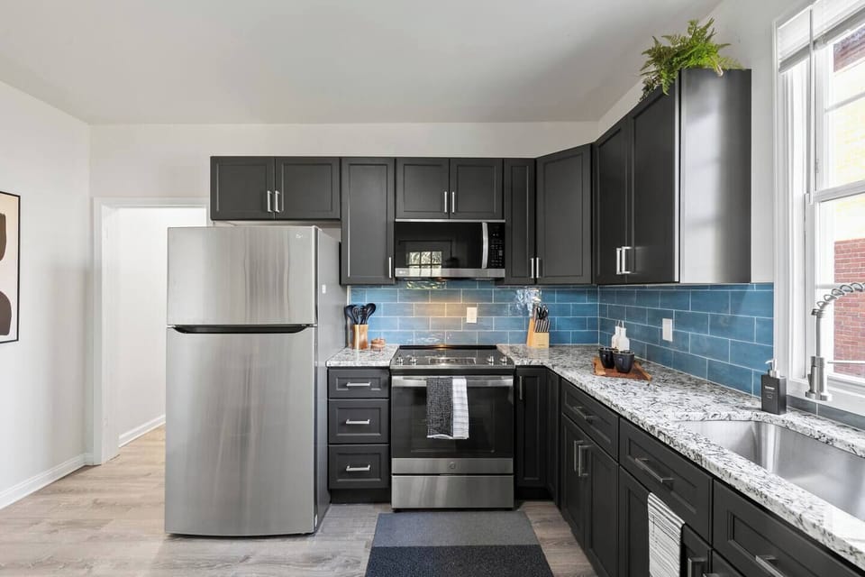 Modern, fully-equipped kitchen featuring sleek dark cabinetry, striking blue subway tile backsplash, and a full suite of stainless steel appliances, including a dishwasher. Plenty of counter space for preparing meals!