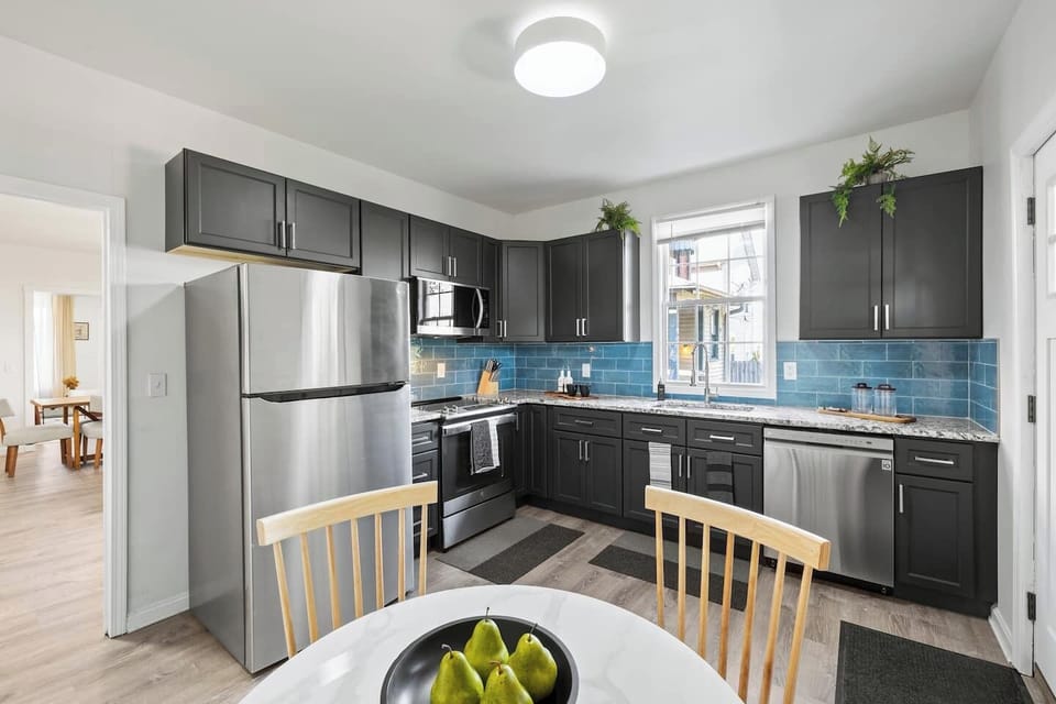 Sleek and modern kitchen with ample counter space and a full suite of stainless steel appliances. The deep grey cabinets and bright backsplash create a modern feel. Perfect for preparing meals and dining in comfort.