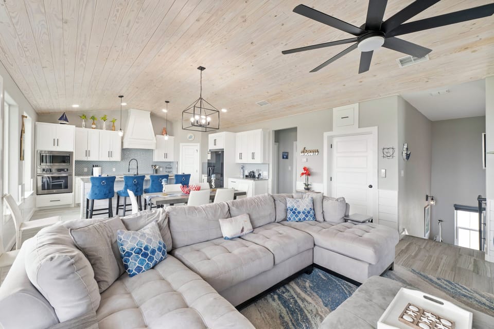 Relax on your plush sectional sofa while the coastal breeze flows through your spacious open-plan living area with modern kitchen.