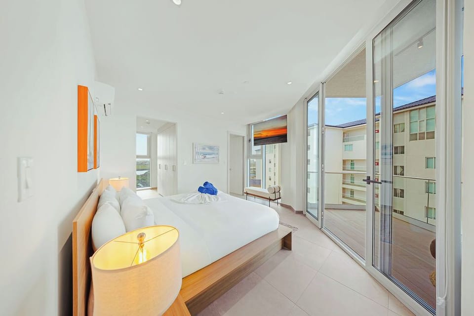 Relax in your bright, airy bedroom with a plush bed and private balcony access. Floor-to-ceiling windows bathe the space in natural light, inviting you to unwind in modern comfort.