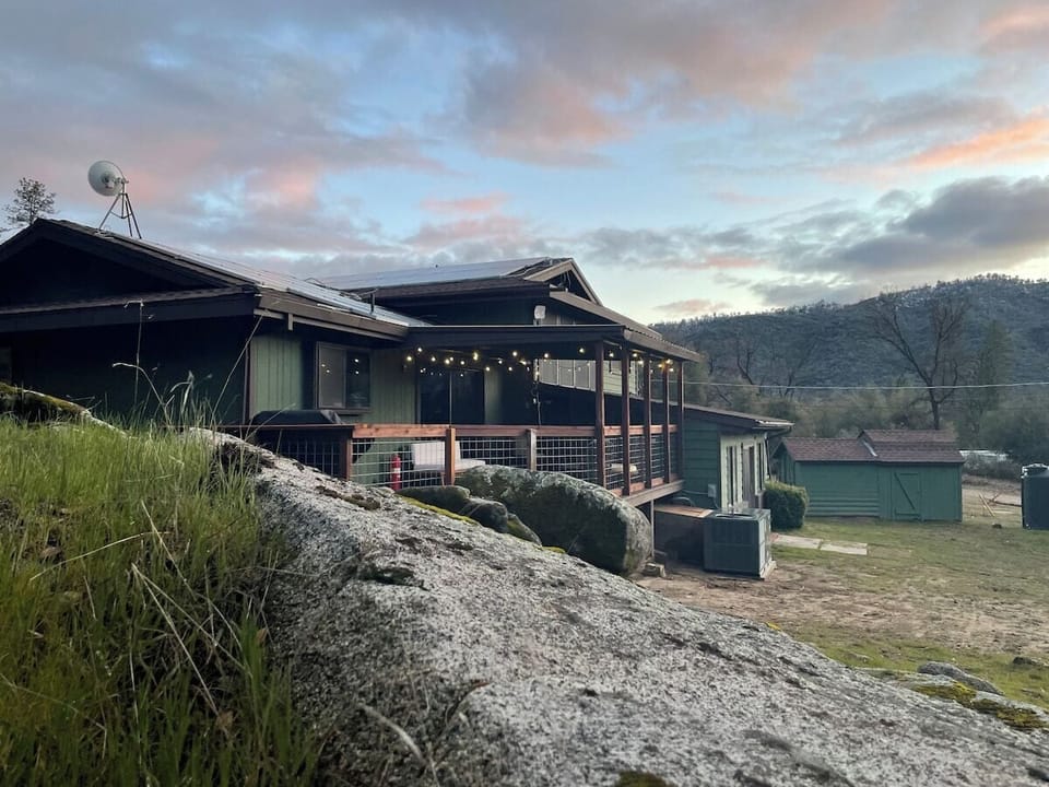 Back view of home. Large deck with grill and cushioned chairs and ottomans.