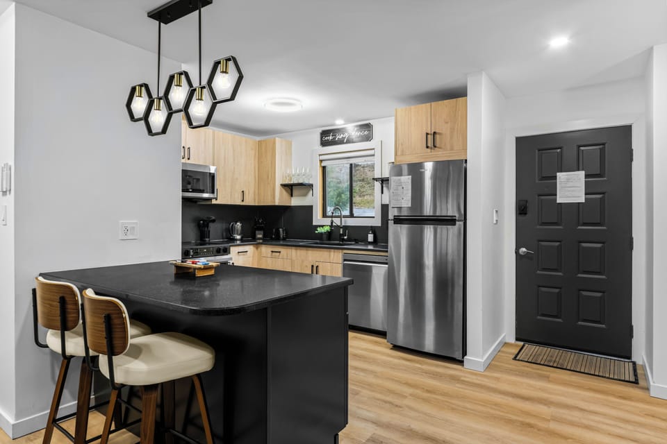 Pull up a stool at the sleek black kitchen island! This renovated culinary space features comfortable breakfast bar seating under chic geometric pendant lights, stainless steel appliances, and a seamless flow to the main townhouse entry.