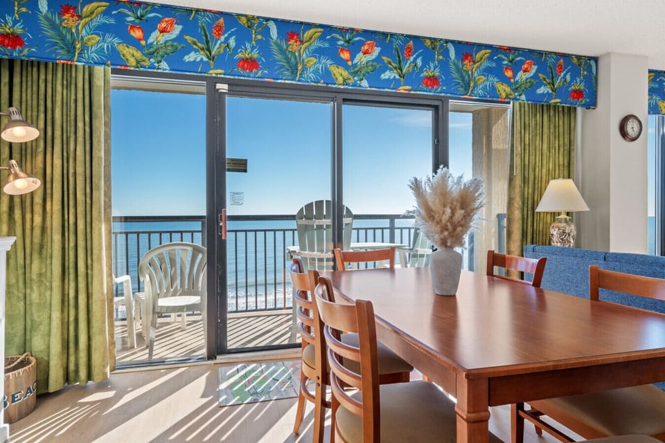Oceanfront dining area in North Myrtle Beach with seating for 6. Floor-to-ceiling windows showcase stunning coastal views, with direct access to the private balcony for ocean breezes and outdoor dining.