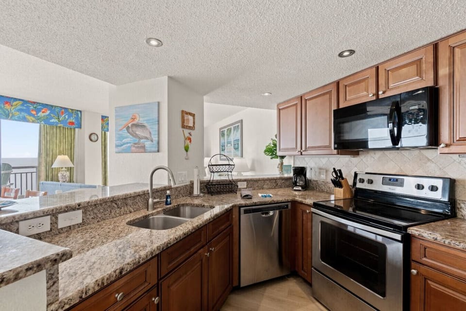 Modern oceanfront kitchen offering full appliances, generous cabinet storage, and sweeping ocean views. Equipped with a stove, oven, microwave, refrigerator with freezer, cookware, dishware, and both Keurig and drip coffee makers.