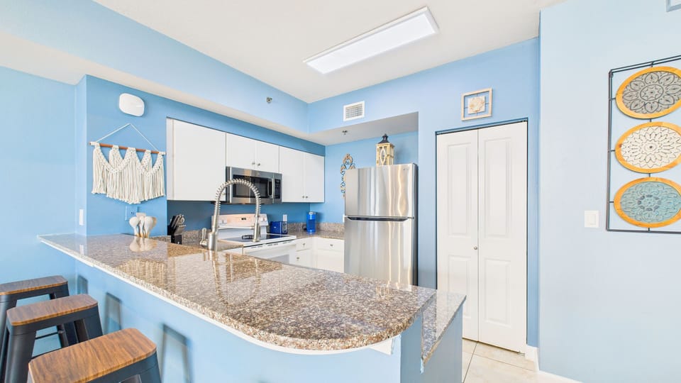 Relax in this bright coastal kitchen where ocean blues meet modern convenience, complete with granite counters and stainless appliances for your comfort.