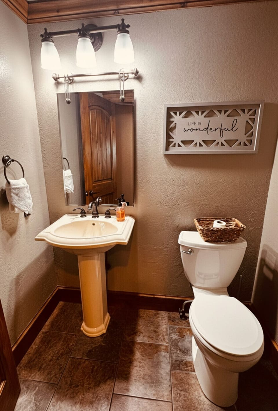 Cozy rustic half-bath with pedestal sink, warm lighting, and charming cabin-style decor — perfect for a comfortable mountain retreat stay