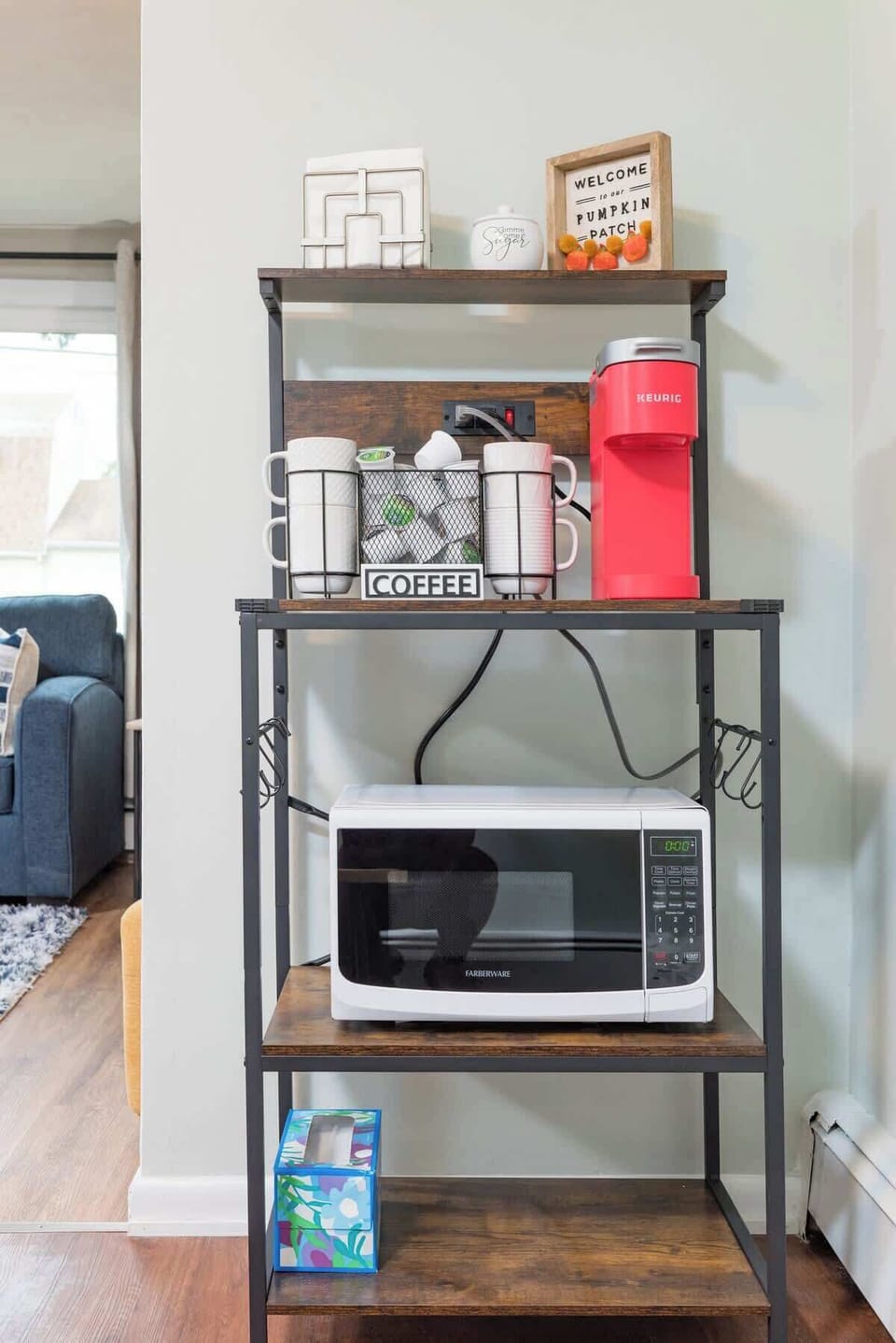 This is a kitchen shelf that serves as a coffee station with a red Keurig machine and a selection of mugs. Below the coffee station is a microwave oven for quick meals. The shelf is practical for everyday use 