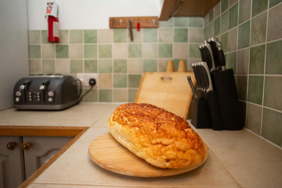 Bread loaf on cutting board beside knife block and toaster