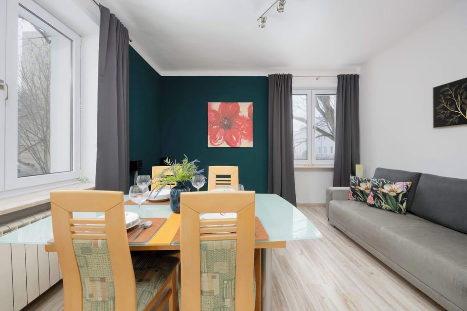 A dining space viewed from another angle, showing the table near the window and green walls. Curtains soften the daylight entering the room. The area feels comfortable and well balanced.