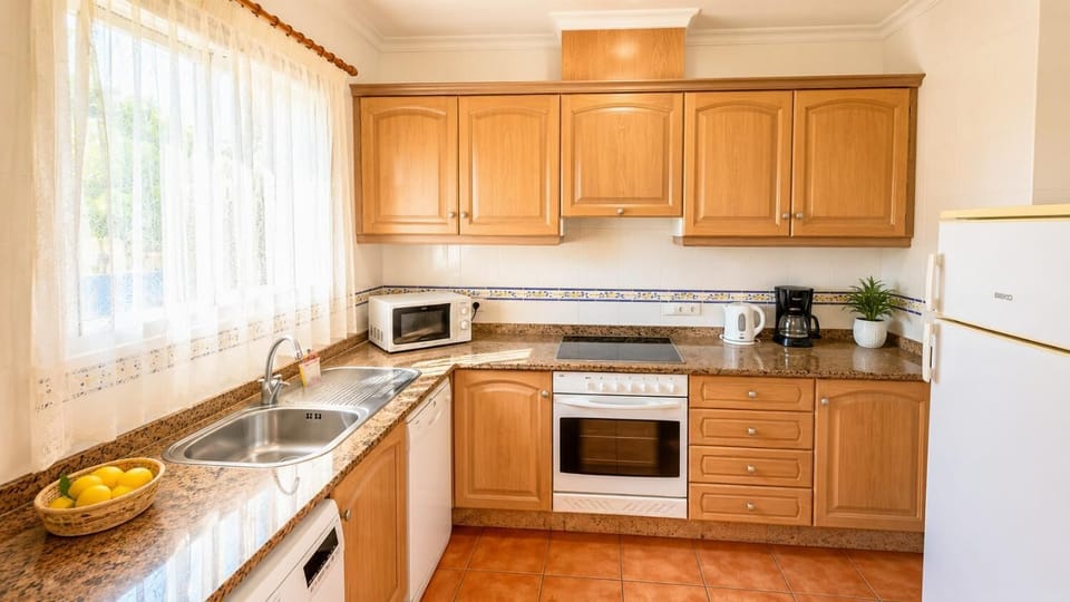 Fully equipped villa kitchen with wooden cabinets and white appliances.
