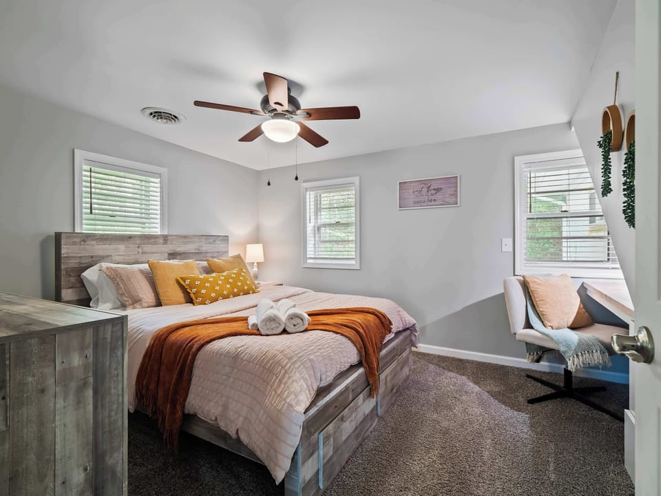Bright bedroom w/ soft tones, ceiling fan & cozy seating area for relaxed evenings