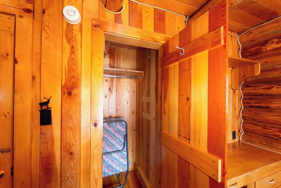 Unpack and settle into warm cabin-style storage with natural wood walls, open wardrobe space, and rustic hooks—everything you need to feel right at home.