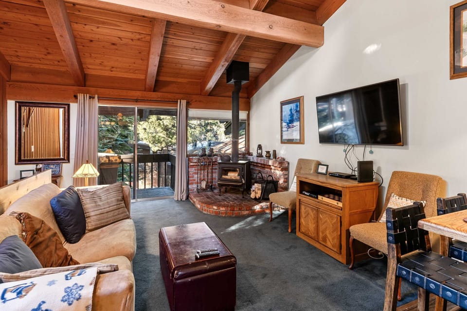 Open living area with vaulted wood ceilings, a cozy wooden fireplace, and a private balcony.