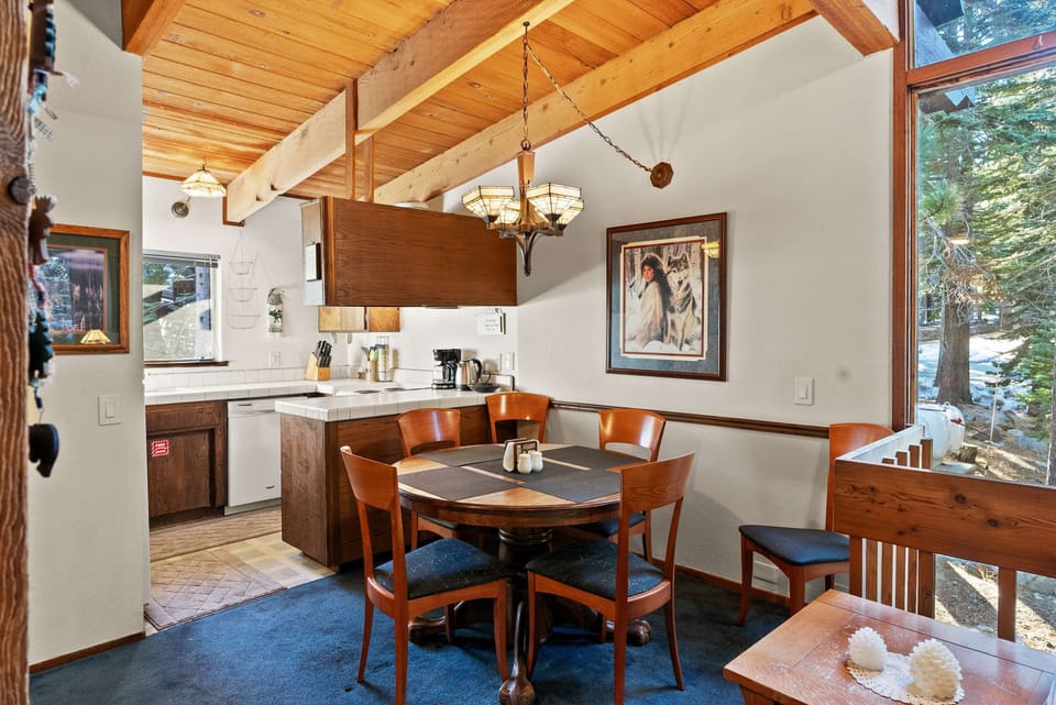 Sunny dining area with a round table for four and floor-to-ceiling forest views.
