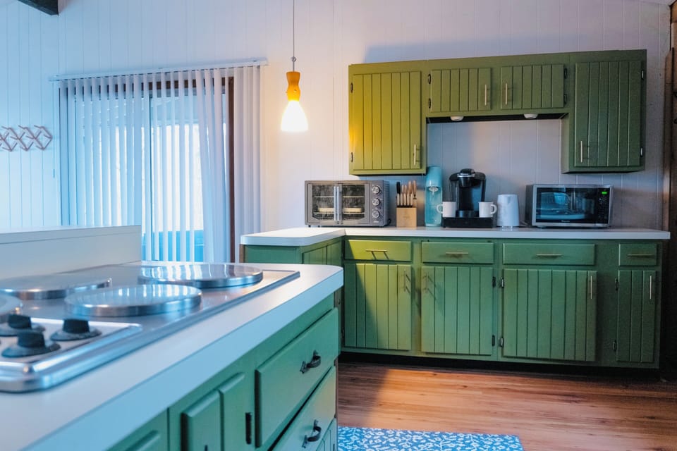 Retro kitchen with green cabinets, modern appliances, and plenty of light.