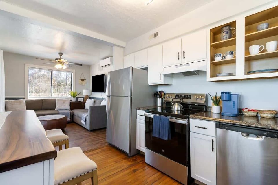 A fully equipped kitchen featuring stainless steel appliances, white cabinets, and an open layout connecting to the living area. The design blends modern and rustic elements.