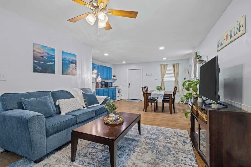 Comfortable blue sofas and beach-themed decor create a warm and welcoming space. The open layout connects seamlessly to the dining and kitchen areas. 