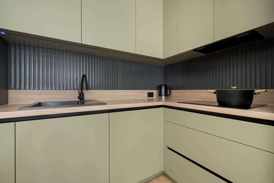 A close-up of a modern kitchen with matte green cabinets and black countertops. Built-in appliances create a clean, streamlined look. The design feels contemporary and elegant.