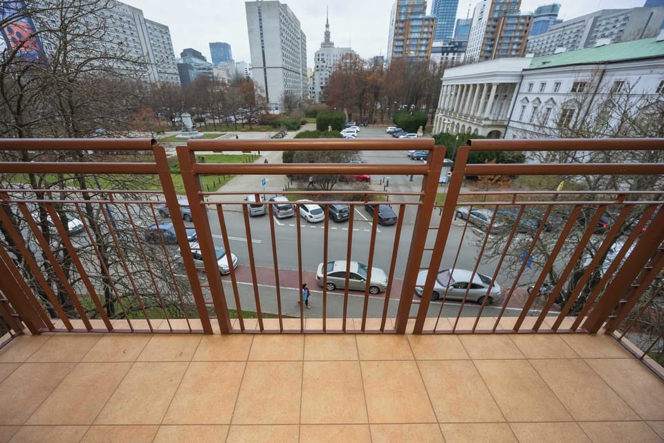 Balcony with wooden floorboards and a view of nearby buildings and city skyline. The space is suitable for relaxing outdoors.