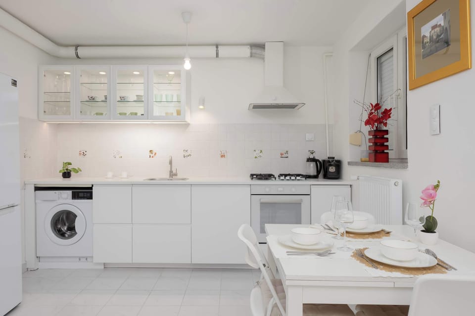 The kitchen area from a different angle showing the dining table and a washing machine in the corner. Large windows bring in natural light.