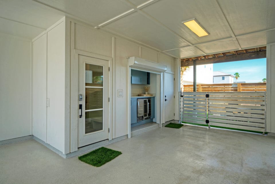 Covered carport featuring a built-in outdoor kitchenette with light blue cabinetry, a sink, and dual beverage refrigerators.